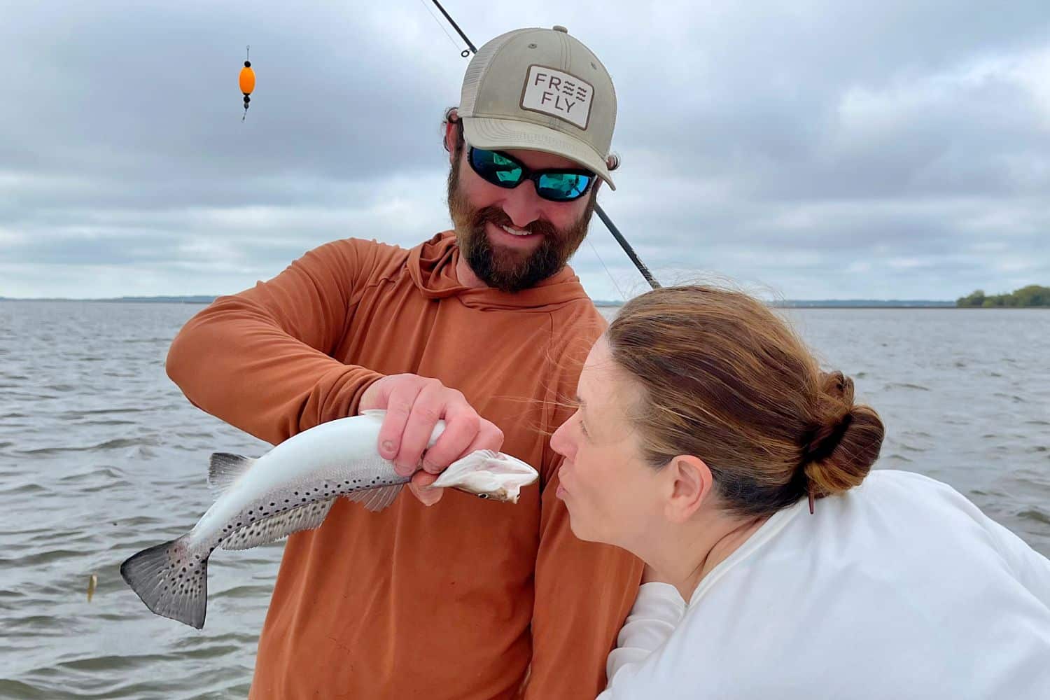 Capt. Nat smiles and jokingly points a fish toward a woman pretending to kiss it