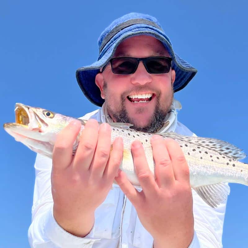 A man wearing a blue hat, holding a fish and smiling
