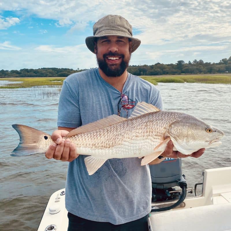 A man holding a large fish standing on a boat
