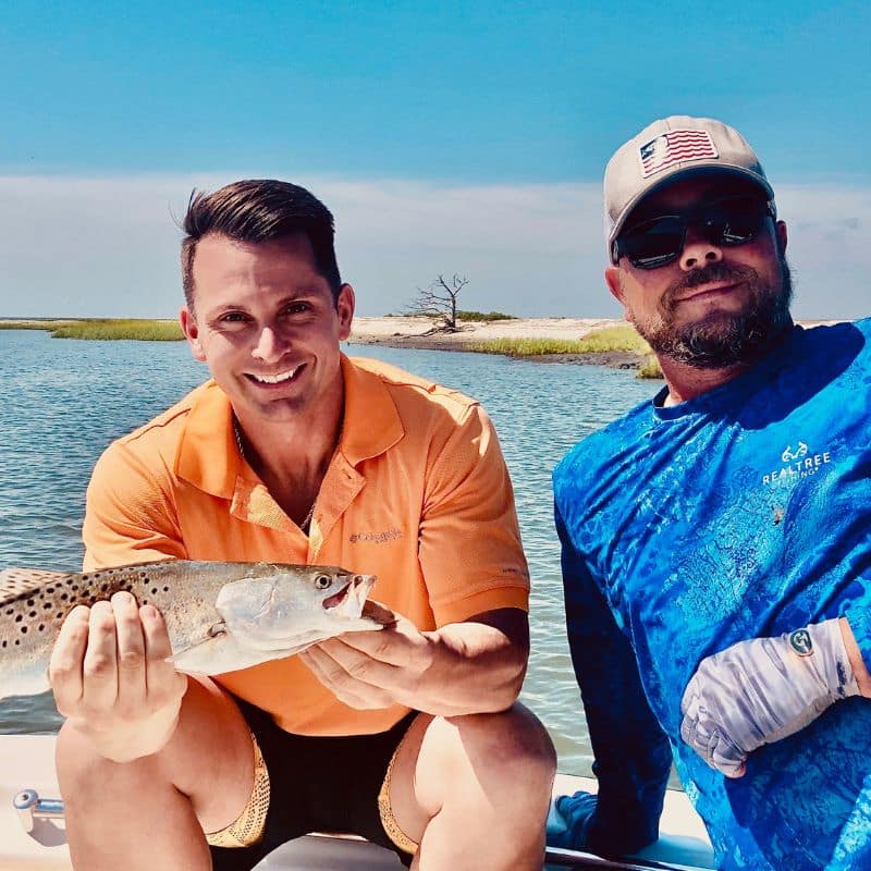 Two men holding fish and smiling while aboard a boat