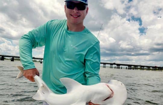 A man proudly holds a shark with waterway in the background